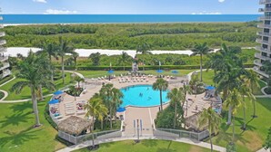 Ein Resort mit einem zentralen Pool, umgeben von Palmen und Liegestühlen, mit Blick auf einen Strand und den Ozean.