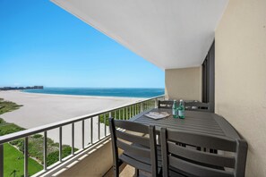A balcony with a table and chairs, overlooking a beach and ocean. - Penthouse Beachfront Condo | Pool/Fitness/Grills (Marco Island)