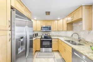 A modern kitchen with stainless steel appliances, wooden cabinets, a granite countertop, and a built-in oven. - Penthouse Beachfront Condo | Pool/Fitness/Grills (Marco Island)