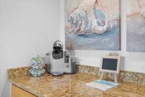 A coffee machine, a coffee pod holder, a chalkboard, and a framed welcome sign on a granite countertop. - Penthouse Beachfront Condo | Pool/Fitness/Grills (Marco Island)