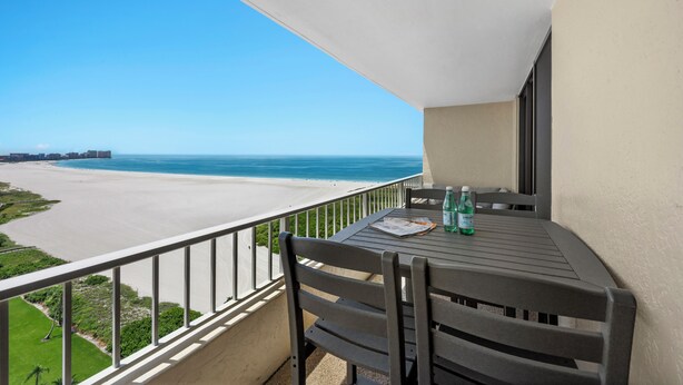 Ein Balkon mit Tisch und Stühlen, der Blick auf einen Strand und das Meer freigibt.