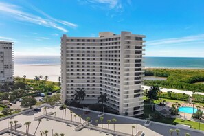 Um hotel alto com várias varandas, uma piscina e vista para a praia e oceano.