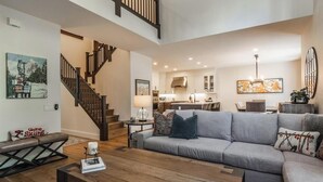 Ein großzügiger Wohnraum mit grauem Sofa, Couchtisch aus Holz und einer Treppe, die in eine obere Ebene führt.