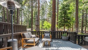 Eine Terrasse mit Sitzgelegenheiten, einem Heizstrahler und Blick auf einen Wald.