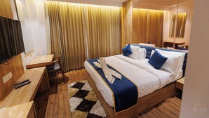 A hotel room with a bed, bedside table, TV, and curtains. - mannat residency by io hotels (Amritsar)