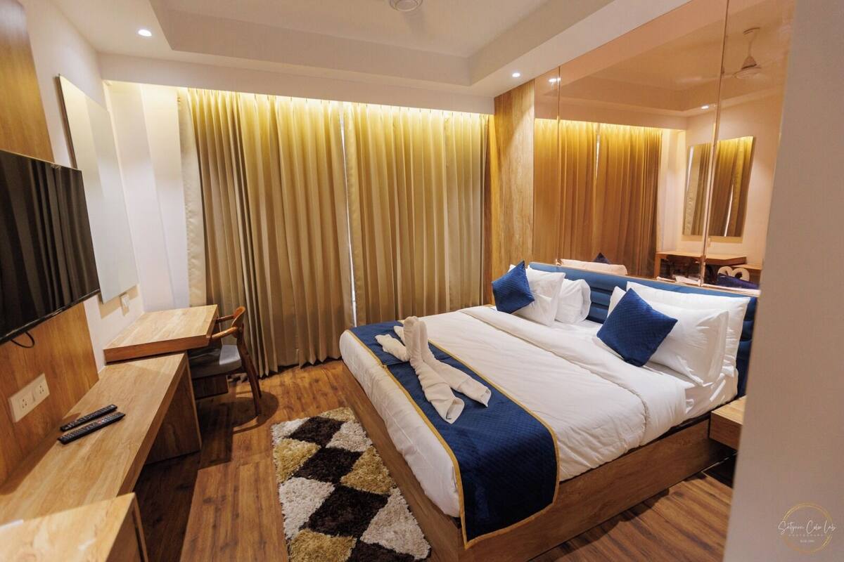 Una habitación de hotel con cama, mesita de noche, televisión y cortinas.
