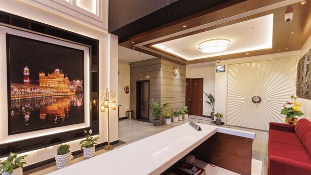 A hotel reception area with a large framed photo of a building, a reception desk, potted plants, a red sofa, and a decorative wall with a radial pattern. - mannat residency by io hotels (Amritsar)