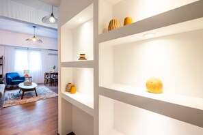 Un salon moderne avec un canapé bleu, une table basse et un coin repas comprenant une table et des chaises. On peut voir des étagères ornées d’objets décoratifs.