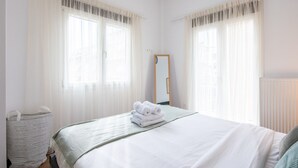 Ett hotellrum med en säng, en spegel och ett fönster med tunna, genomskinliga gardiner.