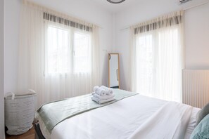 A hotel room with a bed, a mirror, and a window with sheer curtains. - Alex’s 2-Bedroom Apartment in Athens (Greece - Athens)