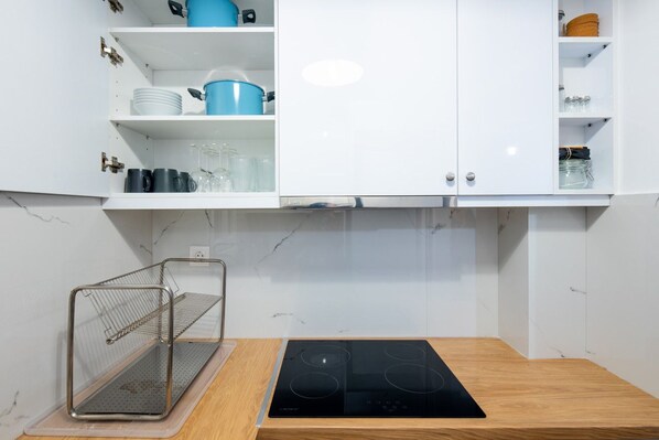 A kitchen with white cabinets, a black induction cooktop, and a metal rack.