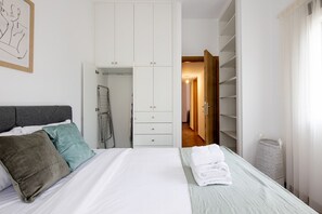 A bedroom with a bed, a wardrobe, and a bathroom visible through an open door. - Alex’s 2-Bedroom Apartment in Athens (Greece - Athens)