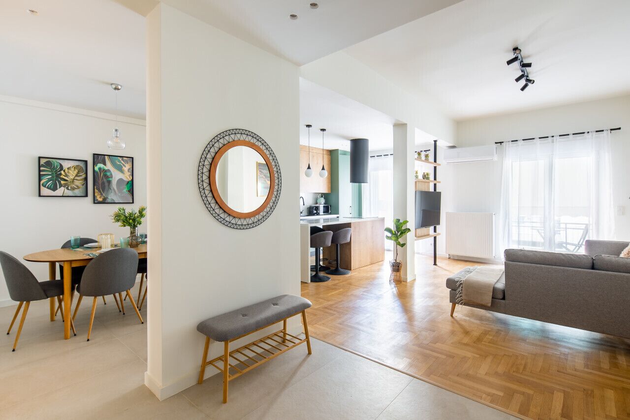 A modern living room with a grey sofa, a wooden bench, and a dining area with a table and chairs.
