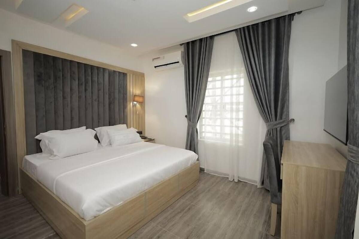 Een moderne hotelkamer met een groot bed, een houten hoofdbord, een nachtkastje, een spiegel en een raam met gordijnen.