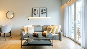 A modern living room with a sofa, a coffee table, and a dining area with a chair and table. - Nova 1-Bedroom Apartment in Athens (Greece - Athens)