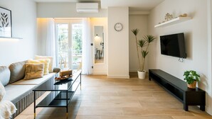 A modern living room with a sofa, coffee table, TV, and plants. - Nova 1-Bedroom Apartment in Athens (Greece - Athens)
