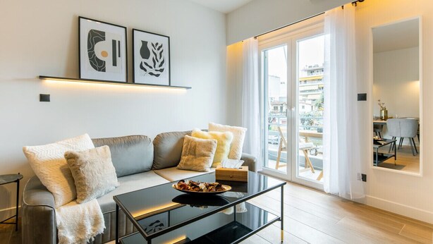 A modern living room with a sofa, a glass coffee table, and artwork on the wall. - Nova 1-Bedroom Apartment in Athens (Greece - Athens)