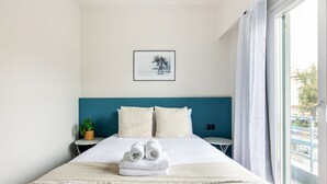 A neatly made bed with white linens, a teal headboard, and a framed picture above it. - Nova 1-Bedroom Apartment in Athens (Greece - Athens)