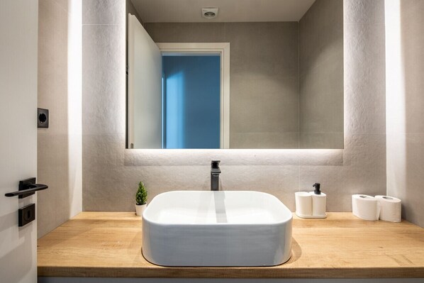 A modern bathroom with a rectangular white sink, a mirror above it, and a wooden countertop.