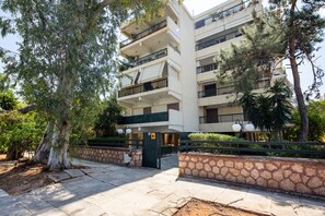 Un edificio residencial de varios pisos con balcones, entrada protegida por una reja y vegetación circundante.