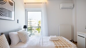 A hotel room with a bed, a radiator, a window with curtains, and a view of the outside. - Bloom - Luxury 2-Bedroom Apartment in Athens (Greece - Glyfada)