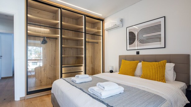 A modern bedroom with a large bed, a walk-in closet, and a framed abstract artwork on the wall. - Bloom - Luxury 2-Bedroom Apartment in Athens (Greece - Glyfada)