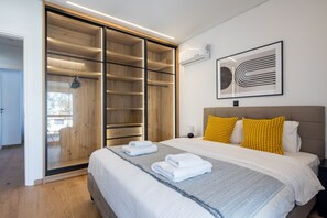 Quarto moderno com uma cama grande, um closet espaçoso e uma obra de arte abstrata emoldurada na parede.