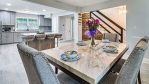 Une cuisine moderne avec des meubles gris, un îlot en marbre et un coin repas comprenant une table en marbre et des chaises grises à revêtement.