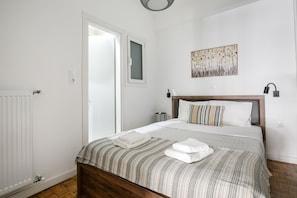 Un dormitorio con cama, radiador, puerta, luz empotrada en la pared y un cuadro.