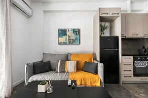 Un salon moderne comprenant un canapé, une table basse et un coin cuisine avec des placards et un réfrigérateur.