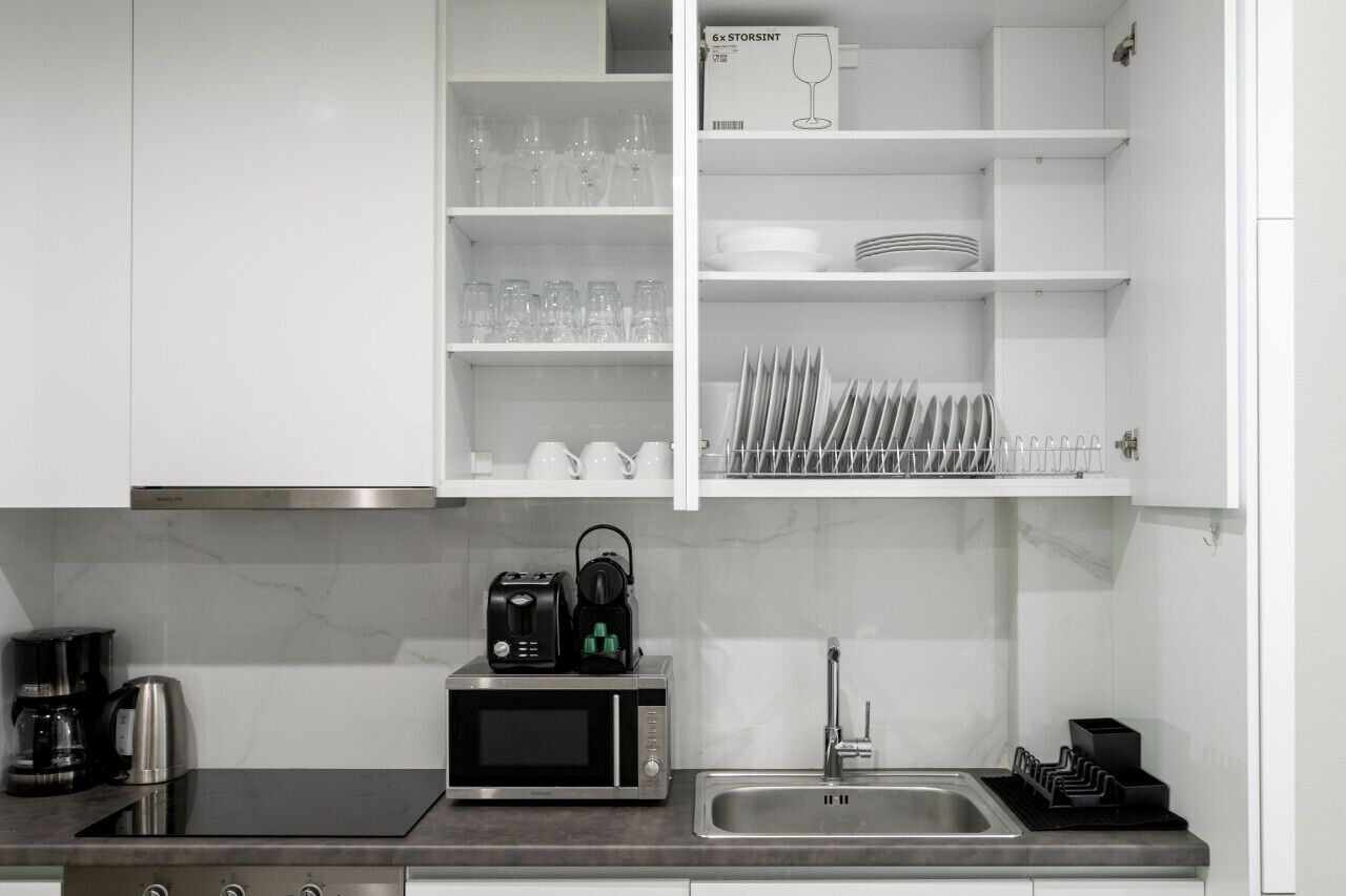 Una cocina moderna con armarios blancos, microondas, cafetera y espacio para guardar copas de vino.