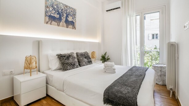A modern bedroom with a large bed, a bedside table, a nightstand, a wall-mounted air conditioner, and a window with curtains. - Mellow 2-Bedroom Apartment in Athens (Greece - Athens)