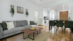 A modern living room with a grey sofa, a wooden coffee table, and a dining area with a table and chairs. - Mellow 2-Bedroom Apartment in Athens (Greece - Athens)