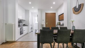 A modern kitchen with white cabinets, a dining area with a wooden table and black chairs, and a visible door leading to another room. - Mellow 2-Bedroom Apartment in Athens (Greece - Athens)