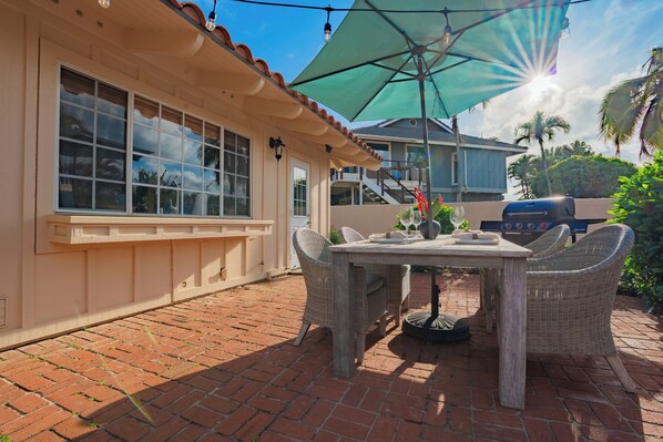 A patio with a table and chairs, a grill, and a large umbrella.
