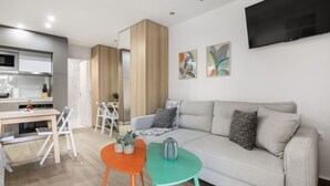 Un salon moderne avec un canapé, deux petites tables et un téléviseur fixé au mur.