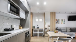 Une cuisine moderne équipée d’un four à micro-ondes encastré, un coin repas avec une table et des chaises en bois, et un salon avec un canapé et un téléviseur à écran plat.