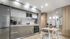 Une cuisine moderne équipée d’un réfrigérateur, d’un four à micro-ondes et d’un four, tous en acier inoxydable. On y trouve une table à manger avec des chaises, ainsi qu’un petit îlot de cuisine doté d’un évier et d’un plan de travail.