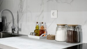 Une cuisine avec un dosseret en marbre, un évier en acier inoxydable et un plateau contenant diverses bouteilles et bocaux.