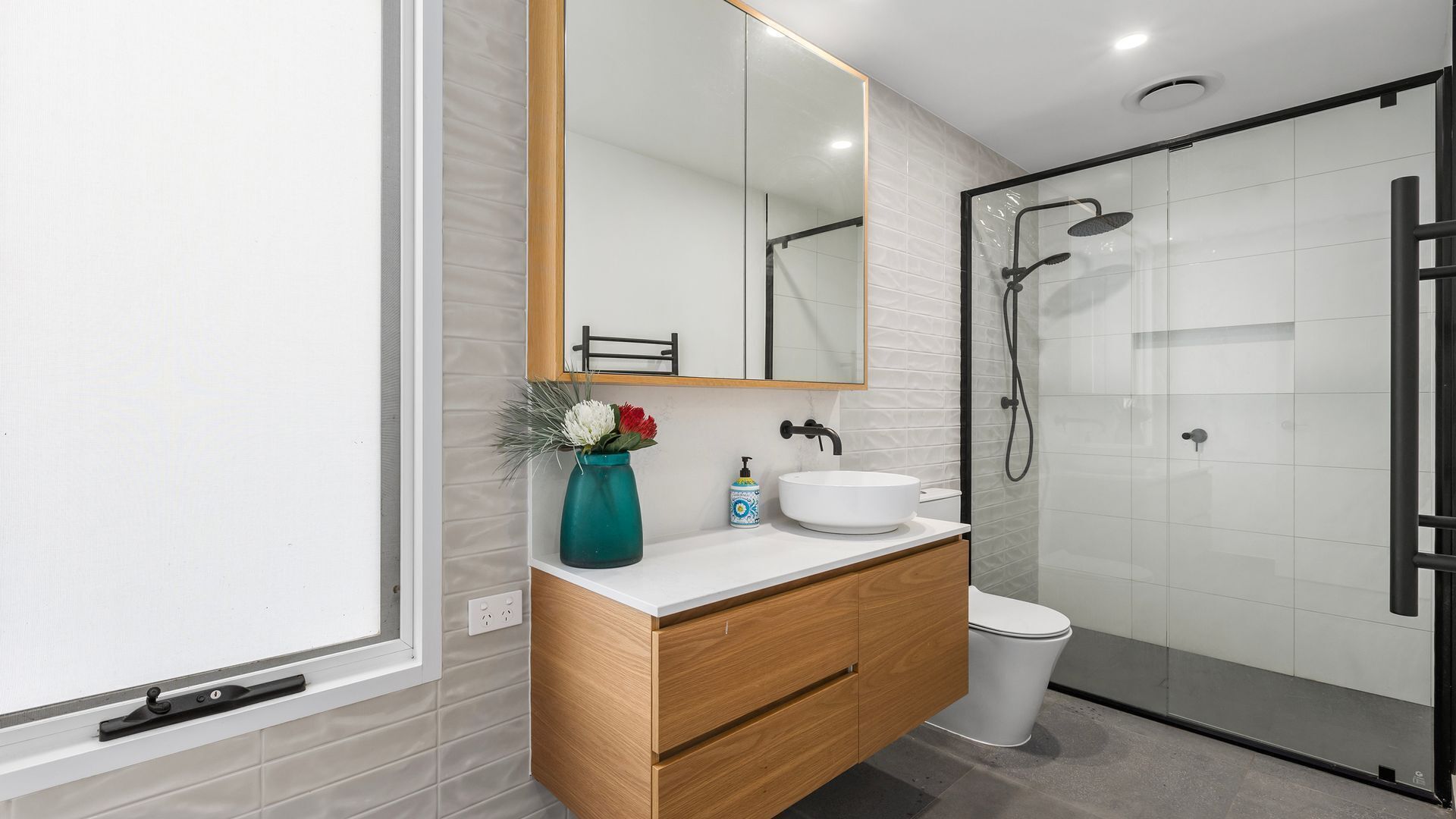 Een moderne badkamer met een houten wastafelmeubel, een wit wastafel en een douchecabine met glazen wanden.