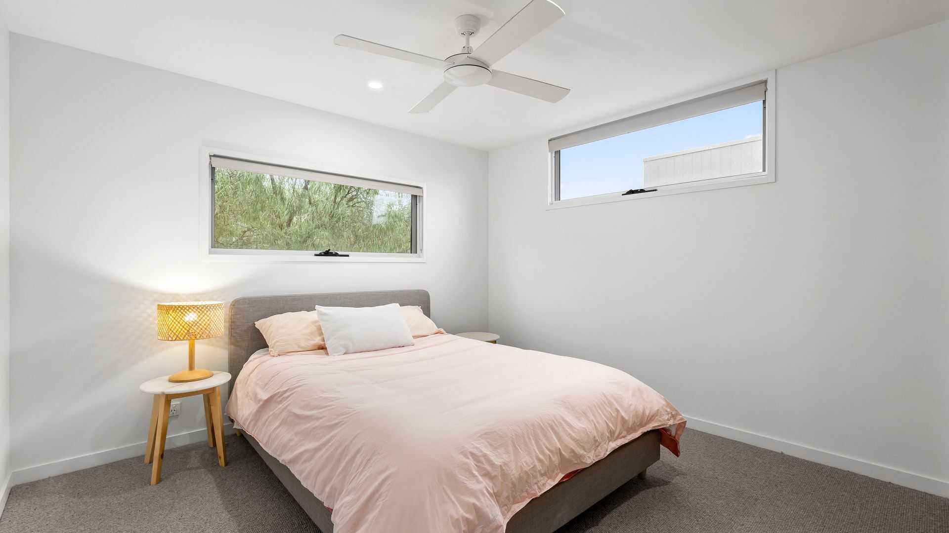 A bedroom with a bed, a nightstand, a lamp, a ceiling fan, and two windows.
