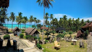 Ein tropisches Resort mit strohgedeckten Hütten, Palmen und freiem Blick auf das türkisblaue Meer.