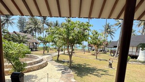 Ein überdachter Patio-Bereich mit Blick auf einen angelegten Garten und einen Strand.