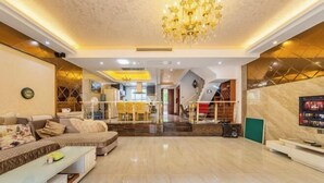 Un amplio salón con una araña, un conjunto de sofás, un televisor y una escalera que sube a otro nivel.