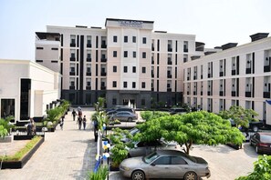 A modern hotel with a central entrance, multiple floors, and a parking area with cars and greenery. - View point Hotel and Suites  (Benin City)