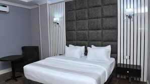 A modern hotel room with a large bed, a chair, a small table, and a wall-mounted air conditioner. - View point Hotel and Suites  (Benin City)