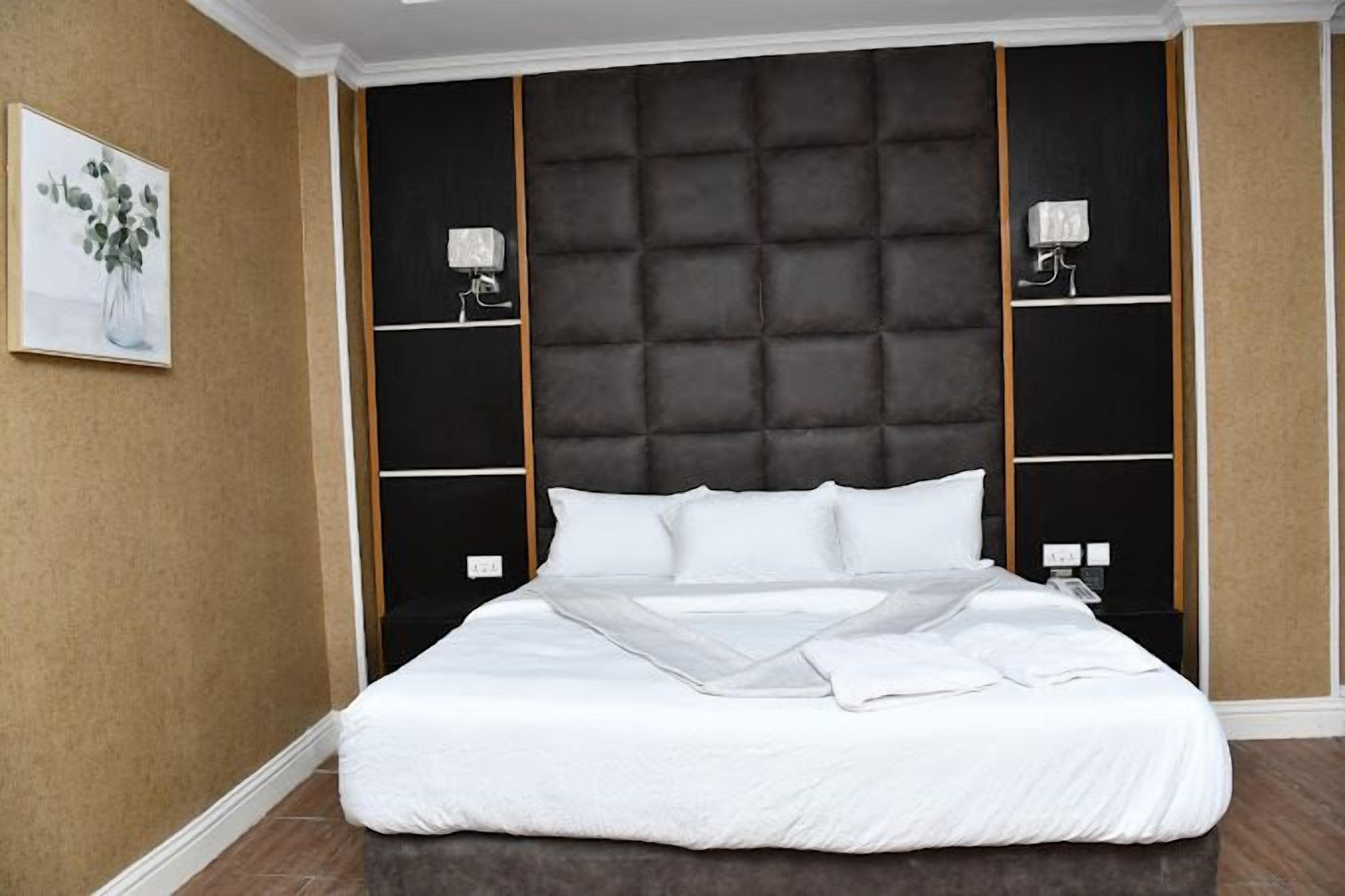 A large bed with a tufted headboard, two bedside tables with lamps, and a framed picture on the wall.