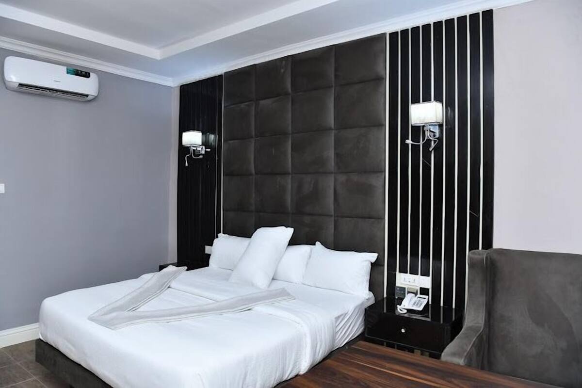 A modern hotel room with a large bed, a dark headboard, and a built-in desk with a telephone.