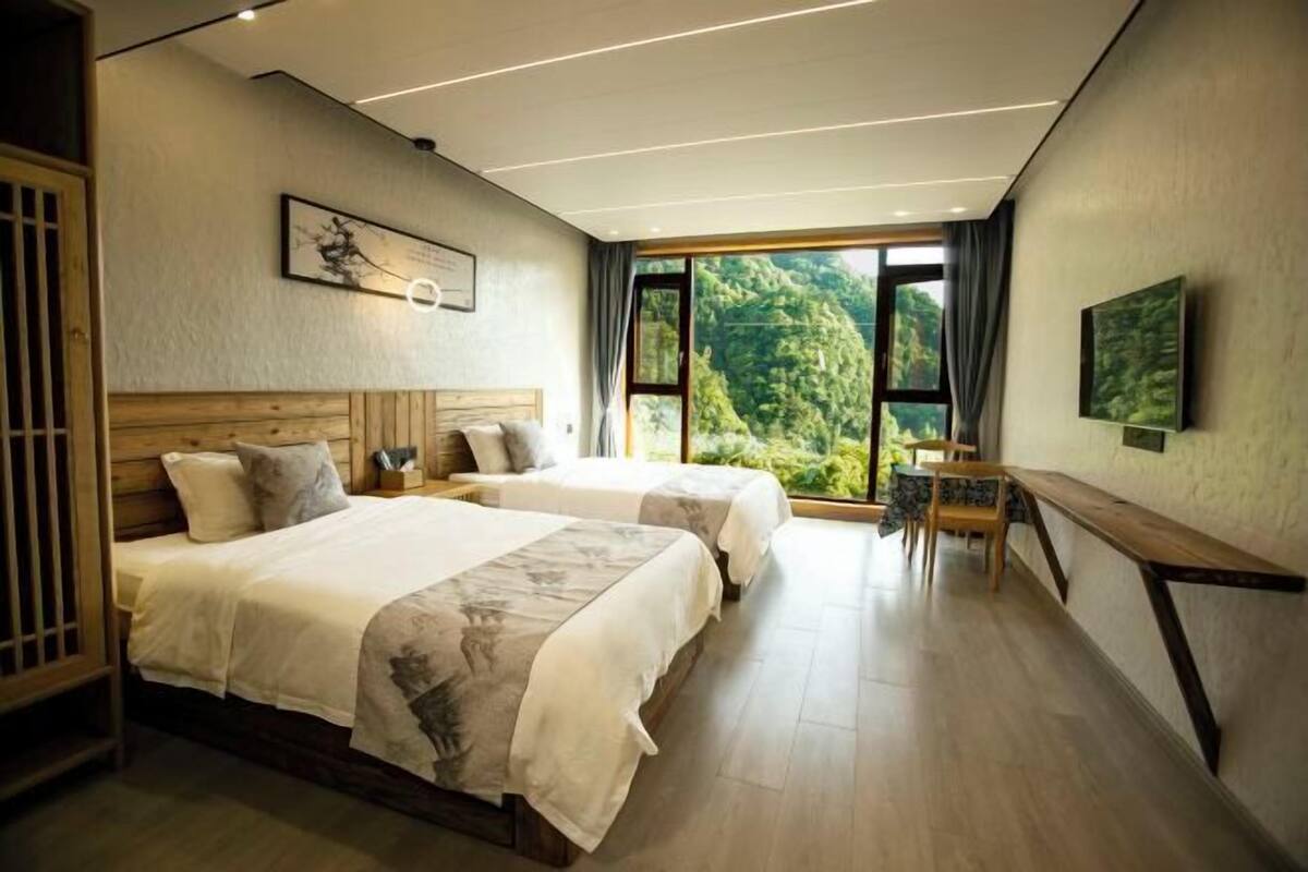 Habitación de hotel moderna con dos camas, un comedor y un gran ventanal con vistas al exterior.