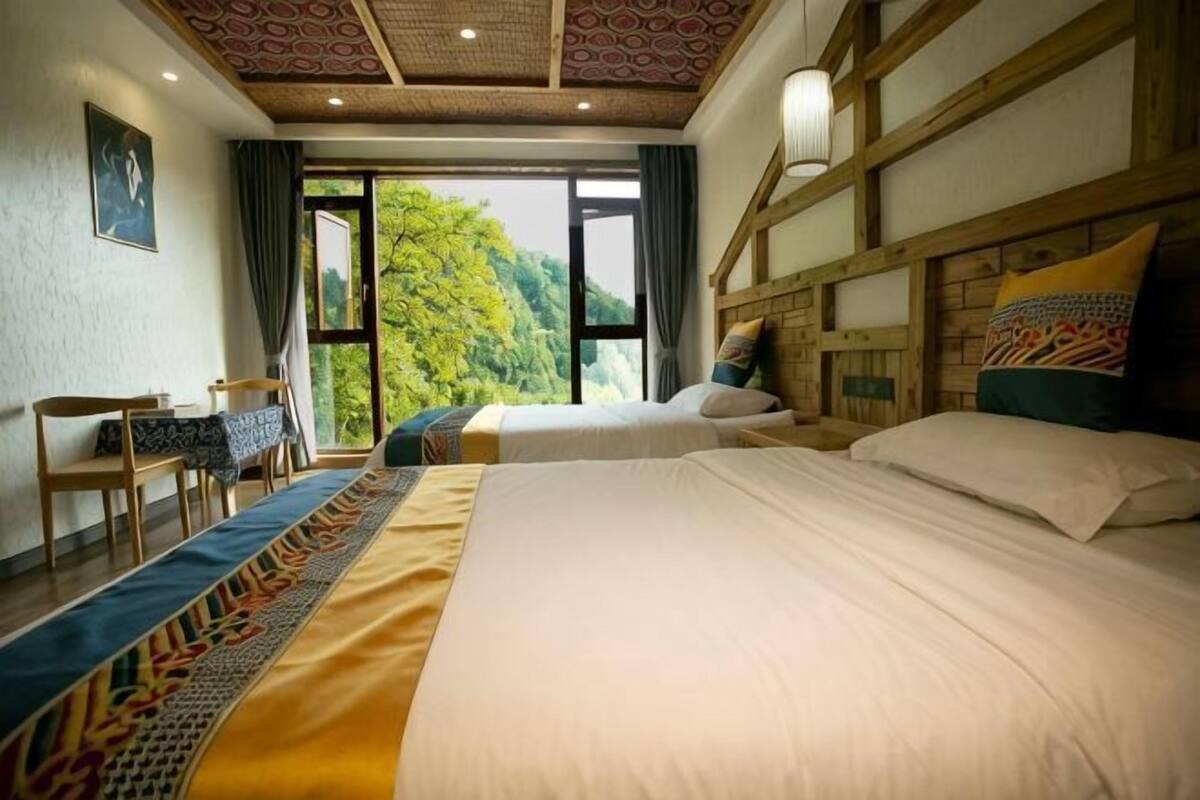 Habitación de hotel con dos camas, un escritorio y vistas a zonas verdes a través de amplios ventanales.